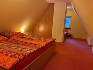 A bedroom with a bed, a wooden wardrobe, a window, and a carpeted floor. - "Ferienhaus Antje" directly on the river, Spreewaldhof Schupan in Burg (Spreewald) (Burg (Spreewald))