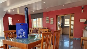 A spacious dining area with a glass table, wooden chairs, and a blue bag on the table.