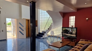 A modern living room with a large flat-screen TV, a sofa, and a staircase leading to an upper level.