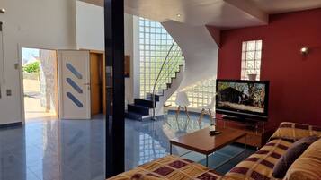 Een moderne woonkamer met een grote flatscreen televisie, een bank en een trap naar een hoger gelegen verdieping.