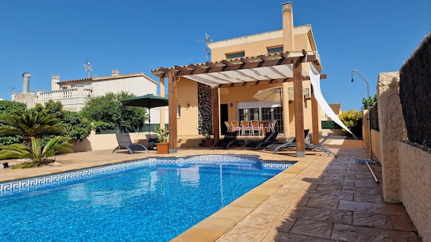 A pool area with a pergola, lounge chairs, and a table with umbrellas.
