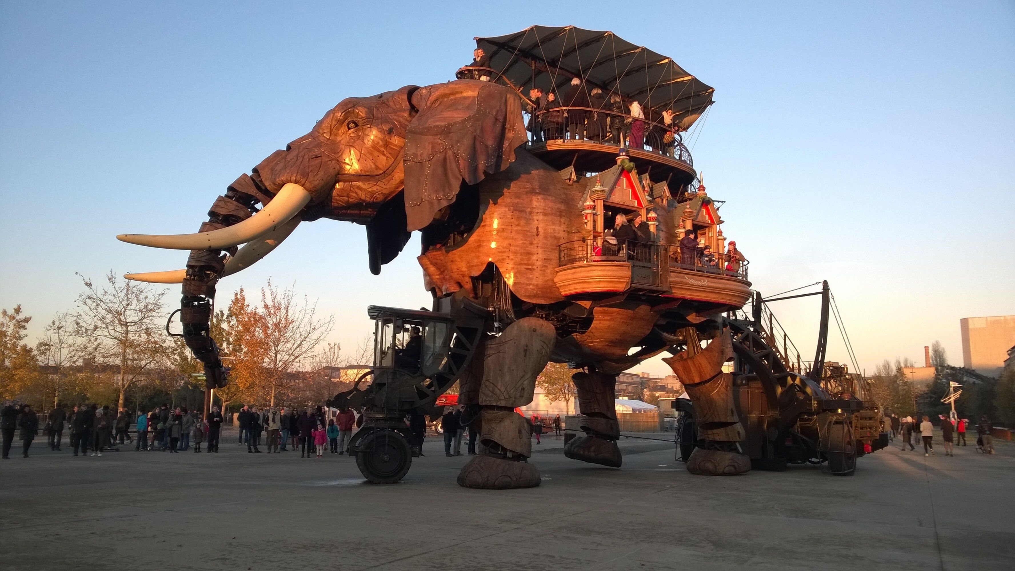 Een grote mechanische olifant met een platform op de rug, omringd door een menigte.