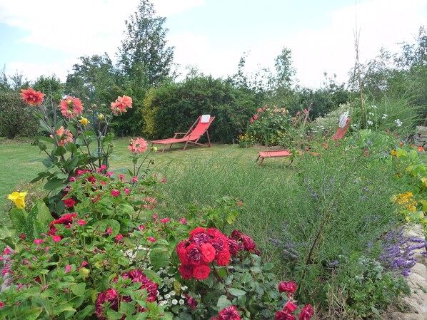 A garden with various flowers and a red lounge chair. - Gite 37 bis rue du pré de la dame. (Férel)