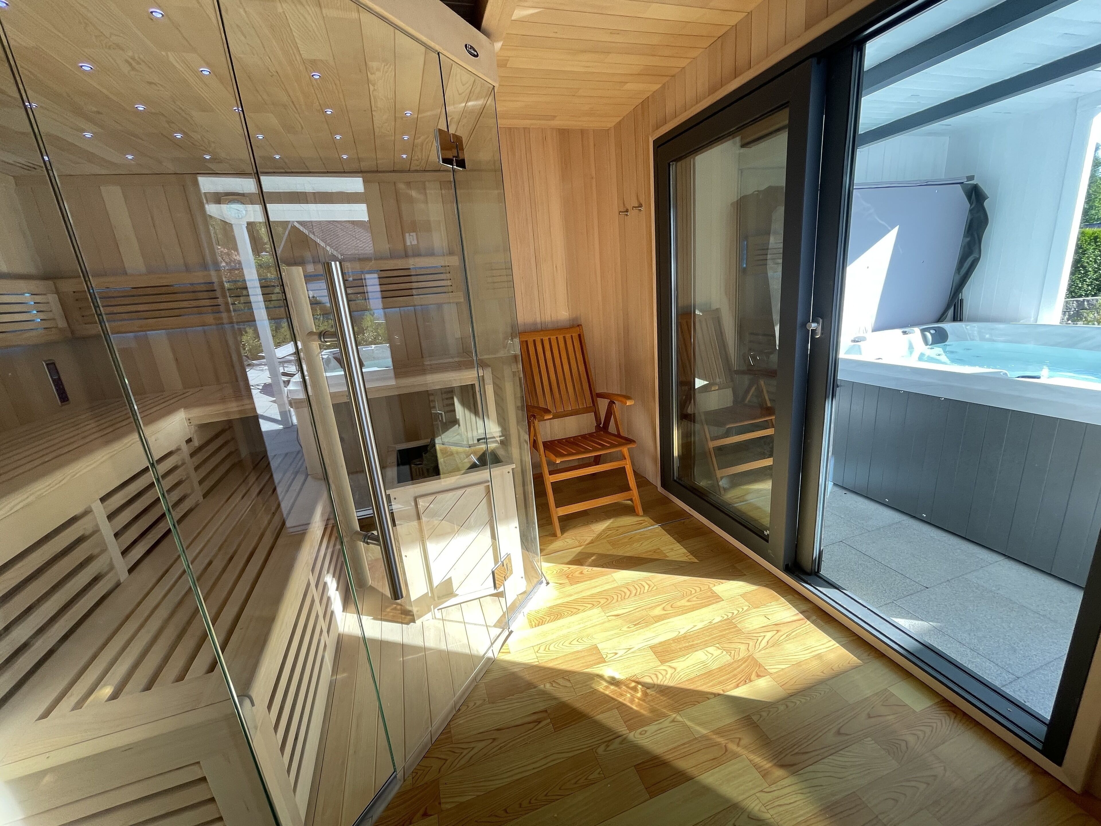 Un intérieur moderne avec un lambris en bois, une porte vitrée donnant sur l’extérieur, une chaise en bois et un jacuzzi visible à travers la vitre.