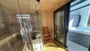 A modern interior with wooden paneling, a glass door leading outside, a wooden chair, and a hot tub visible through the glass. - Cozy cottage with much comfort (Rheinboellen)
