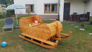 Una casetta gioco in legno con una panchina, un tavolo, una sedia e un ombrello in un giardino.