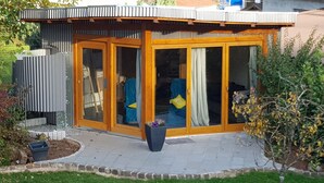Una casa moderna con facciata in legno, ampie porte scorrevoli in vetro e un piccolo giardino.