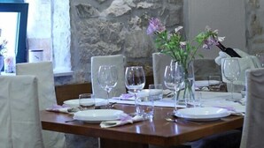 Un coin repas avec un mur en pierre, une table en bois dressée pour quatre personnes, des chaises blanches et un luminaire suspendu.