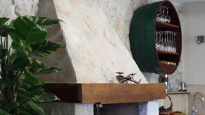 Une cheminée en pierre avec une cheminée en bois, une étagère en forme de tonneau vert au-dessus, et un pot de fleurs sur le côté gauche.
