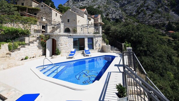 Un bâtiment en pierre doté d’une piscine, de chaises longues et surplombant un paysage montagneux.