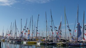 Un port de plaisance où sont amarrés de nombreux voiliers, dont certains arborent des drapeaux, et où l’on peut voir une grande publicité pour la Banque Populaire.
