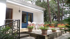 Un bâtiment blanc avec une porte bleue, des plantes en pot et des chaises en plastique blanches à l’extérieur.