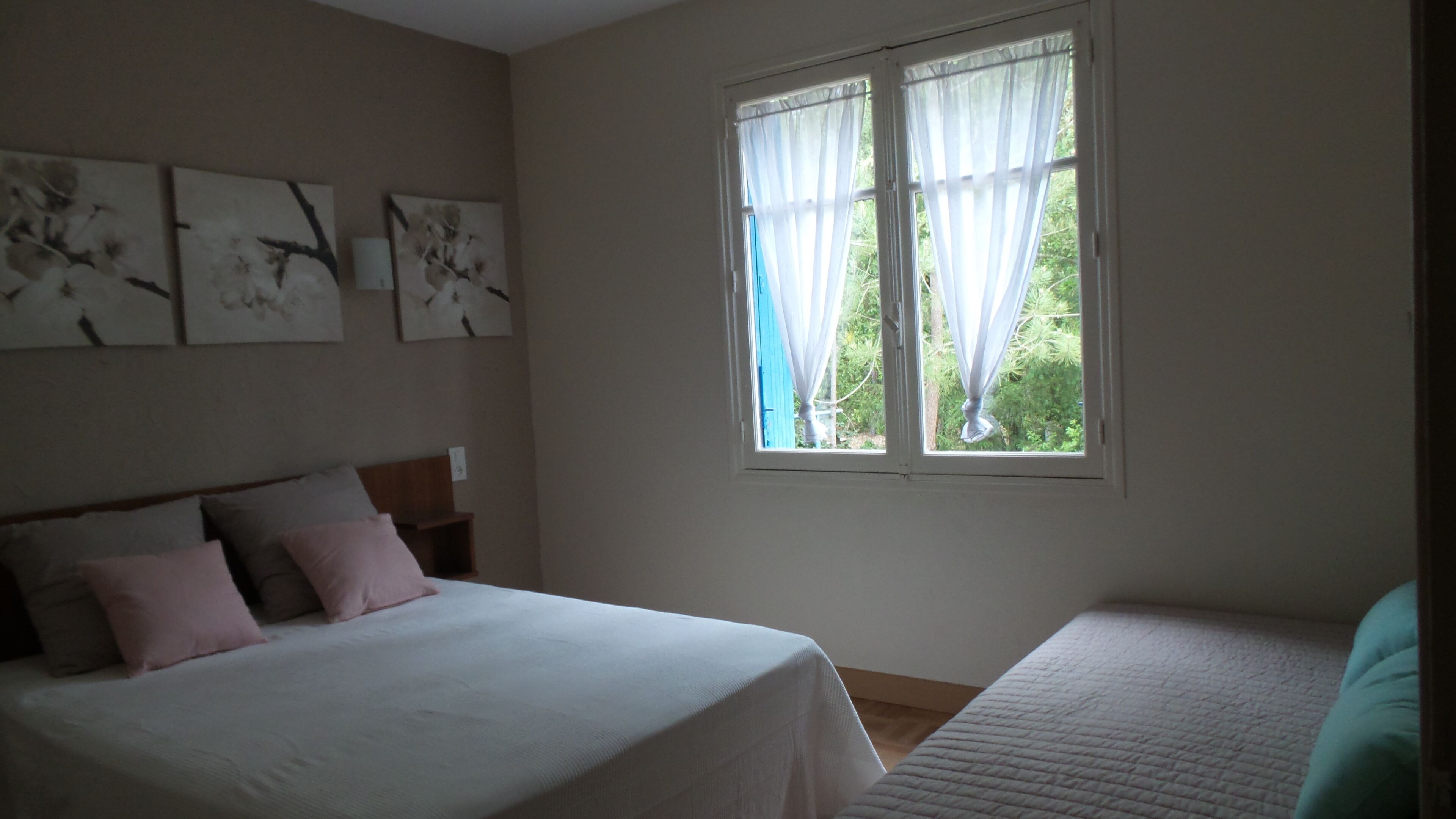 Une chambre à coucher avec un lit, une table de chevet, une fenêtre avec des rideaux et des œuvres d’art murales.