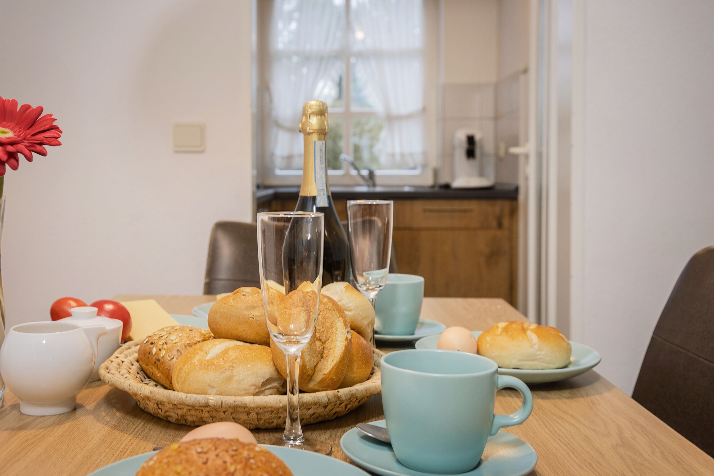 A breakfast setting with bread, eggs, and a bottle of champagne on a wooden table.