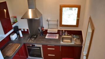 Cucina compatta con piano cottura a gas, forno e lavello in acciaio inossidabile. Sopra il lavello c'è una finestra e nell'angolo una sedia rossa.