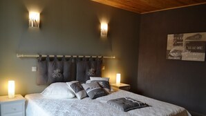 A bedroom with a large bed, two bedside lamps, a headboard with curtains, and a wall-mounted light fixture. - Gite 8 people - forge - Monsegur (Monségur)