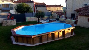 A rectangular wooden pool with a wooden deck surrounding it, set in a backyard with a lawn, a small tree, and a stone wall. - Gite 8 people - forge - Monsegur (Monségur)