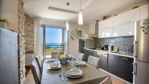 A modern dining area with a table set for four, a kitchen with stainless steel appliances, and a view of the sea through a glass door. - Villa Marino in Makarska, private pool (Makarska)