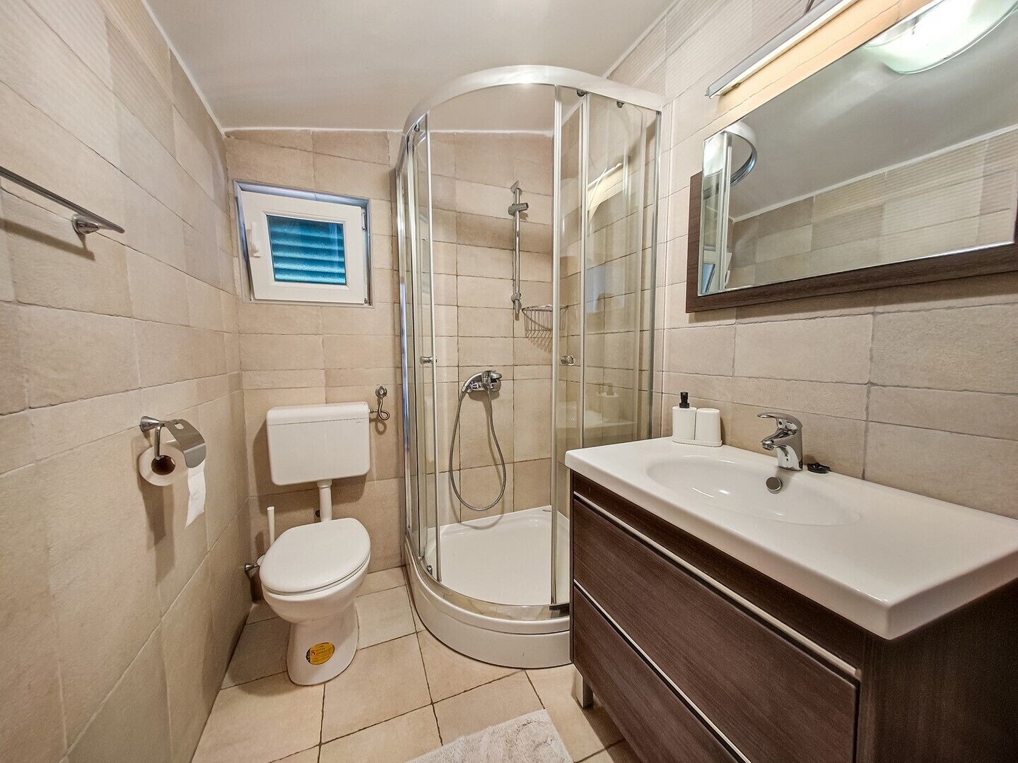 Un baño moderno con ducha de vidrio, inodoro y tocador con lavamanos.