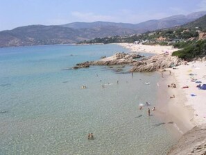Una platja costanera amb aigua cristal·lina, una riba rocosa i persones nedant.