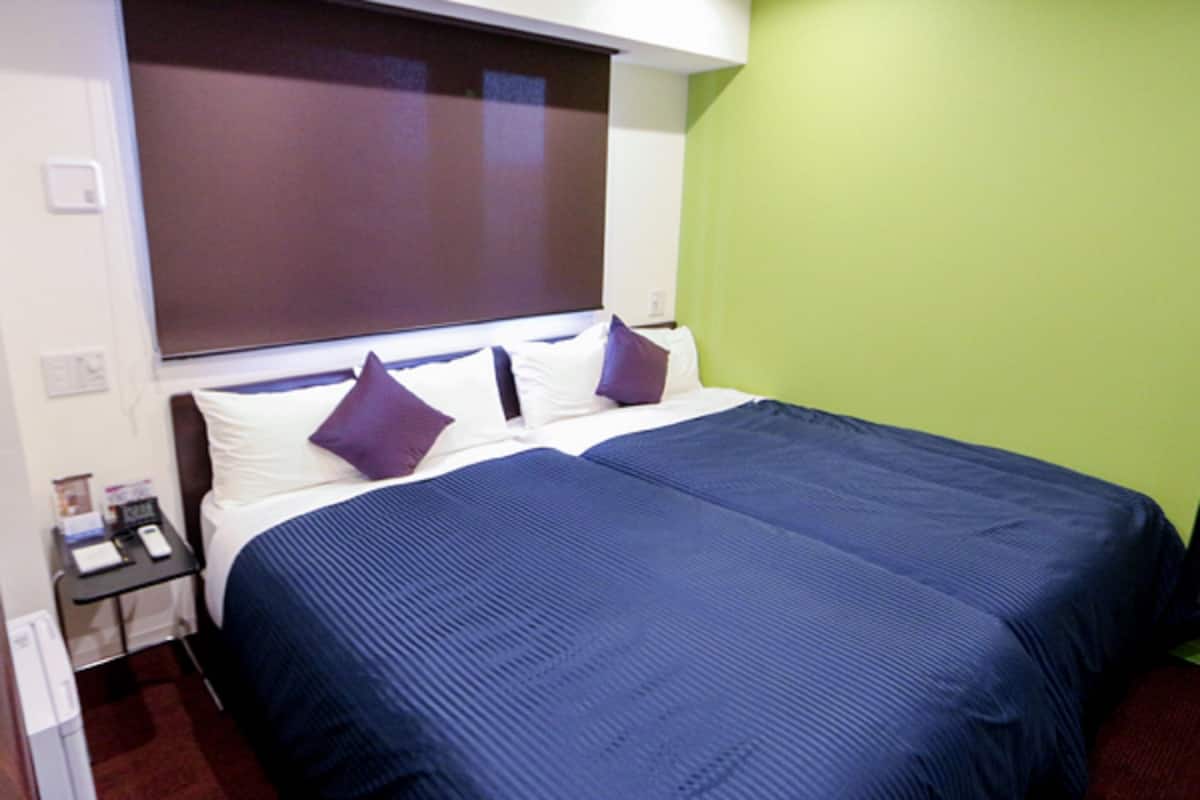 A hotel room with two beds, a nightstand, and a green wall.