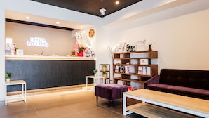 A hotel reception area with a reception desk, a clock, a bookshelf, and a purple sofa. - HOTEL LiVEMAX Ueno-Ekimae (Tokyo)