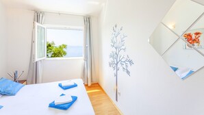 Hotellihuone, jossa on sänky, ikkuna verhoilla, seinälle kiinnitetty peili ja koristeellinen seinätarra, joka esittää puuta.