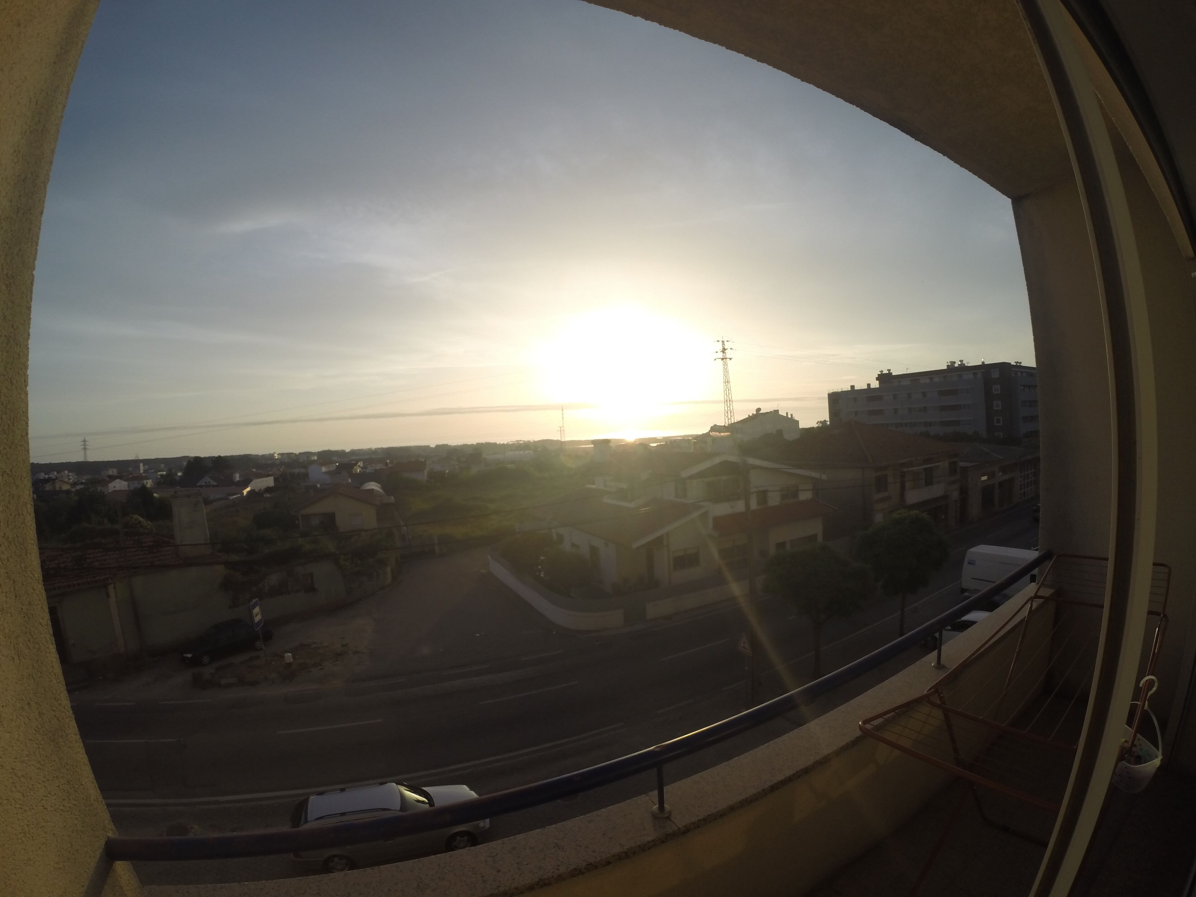 Une vue depuis un balcon, avec un ciel dégagé et le soleil se couchant à l’horizon.