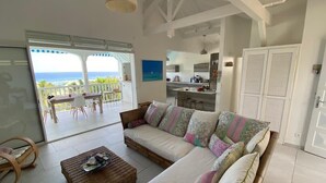 A spacious living area with a sofa, a coffee table, and a view of the ocean through large glass doors. - Panoramic sea view villa - private beach access (Saint-François)