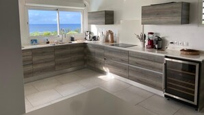 A modern kitchen with a large island, built-in appliances, and a view of the ocean. - Panoramic sea view villa - private beach access (Saint-François)