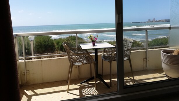 A balcony with a table and chairs, overlooking a beach and ocean.