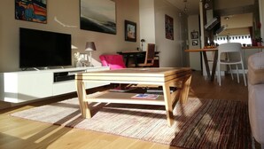 A modern living room with a wooden coffee table, a flat-screen TV, and a dining area with a white chair.