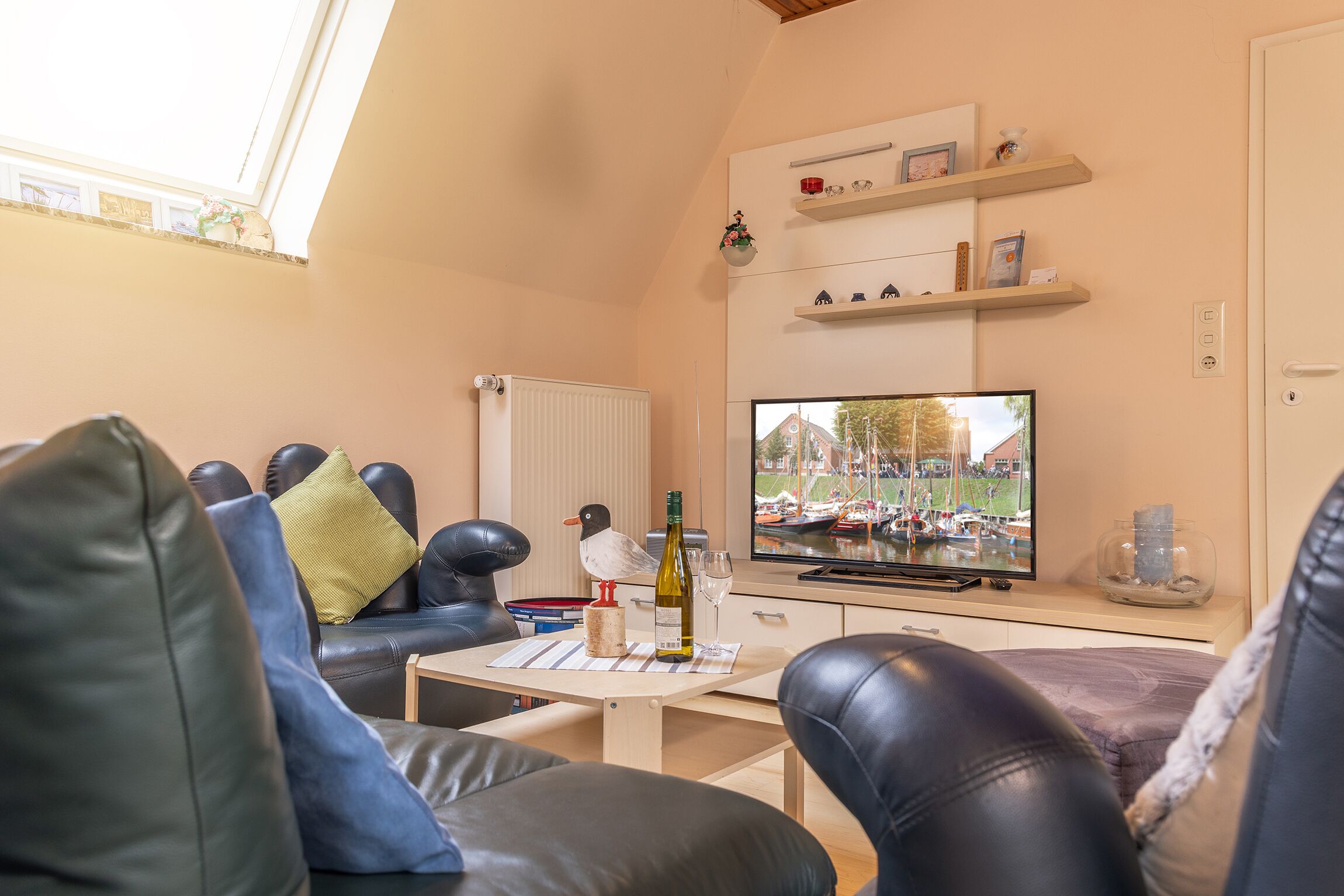Ein gemütliches Wohnzimmer mit Fernseher, Ledersofas, einem Tisch mit Flasche und Gläsern sowie einer Vogelstatue.