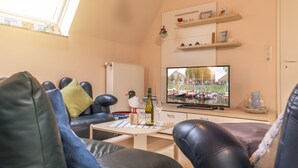 Ein gemütliches Wohnzimmer mit Fernseher, Ledersofas, einem Tisch mit Flasche und Gläsern sowie einer Vogelstatue.