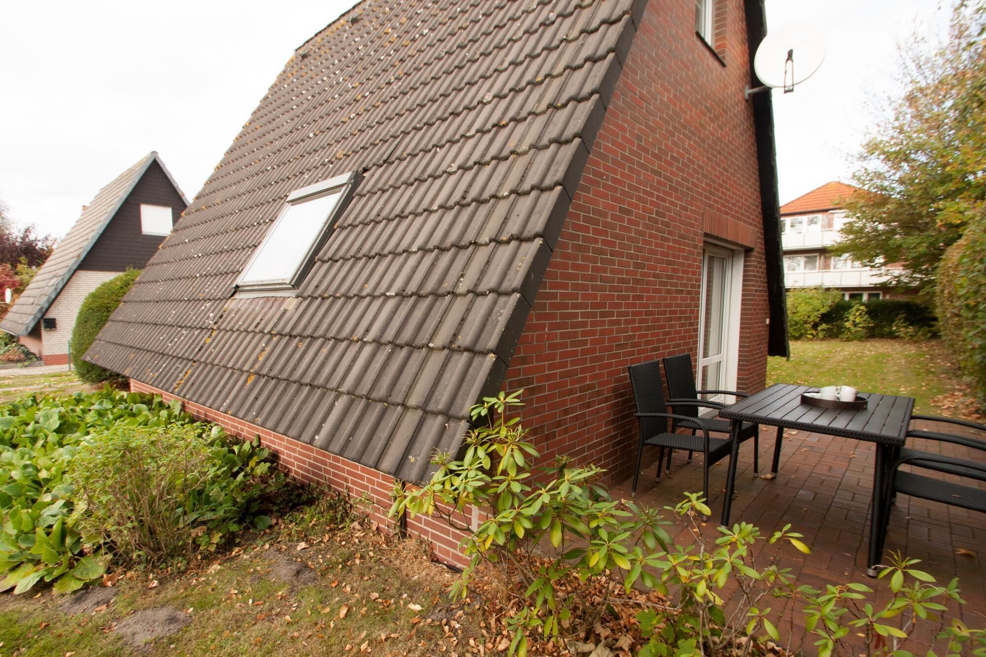 A house with a sloped roof, a brick exterior, and a small patio with a table and chairs.