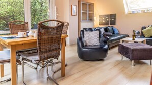 Ein modernes Wohnzimmer mit Essbereich, ausgestattet mit einem Holztisch, Korbstühlen, einem schwarzen Ledersofa und einer Glasvitrine.