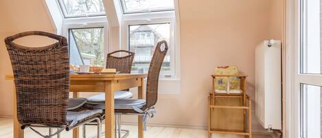 Uma sala de jantar com mesa, cadeiras e janela com vista para uma casa.
