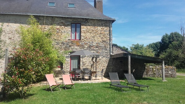 Ein Steinhaus mit Terrasse, das Gartenmöbel und eine überdachte Sitzgelegenheit bietet.