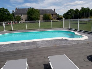 Ein Schwimmbad mit Holzterrasse, umgeben von einem weißen Zaun, und ein Haus im Hintergrund.