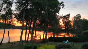 A sunset view over a lake with trees and a hedge in the foreground.
