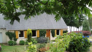 A house with a sloped roof, wooden shutters, and a garden with various plants and flowers.