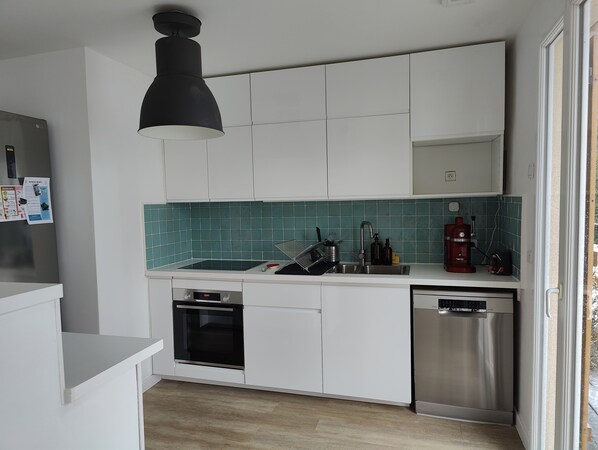 A modern kitchen with white cabinets, a black pendant light, a stainless steel dishwasher, and a tiled backsplash.