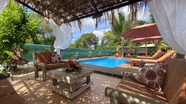 A pool area with lounge chairs, a table with a floral centerpiece, and a covered seating area with a white canopy.