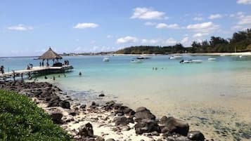 Una spiaggia con acque cristalline turchesi, una struttura con tetto di paglia e imbarcazioni all'orizzonte.
