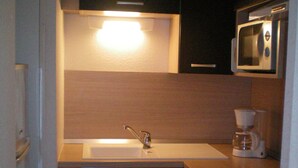 Uma cozinha compacta com pia, cafeteira e micro-ondas.
