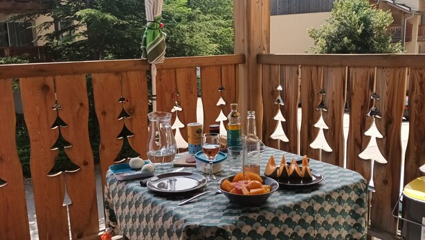 Um deck de madeira com uma mesa posta para refeição, rodeado por uma cerca de madeira com decorações em forma de árvores.