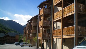 Um edifício com várias andares, varandas, um estacionamento e uma montanha ao fundo.