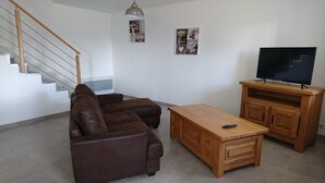 A living room with a brown sofa set, a wooden coffee table, a TV on a wooden stand, and a staircase with a wooden handrail.