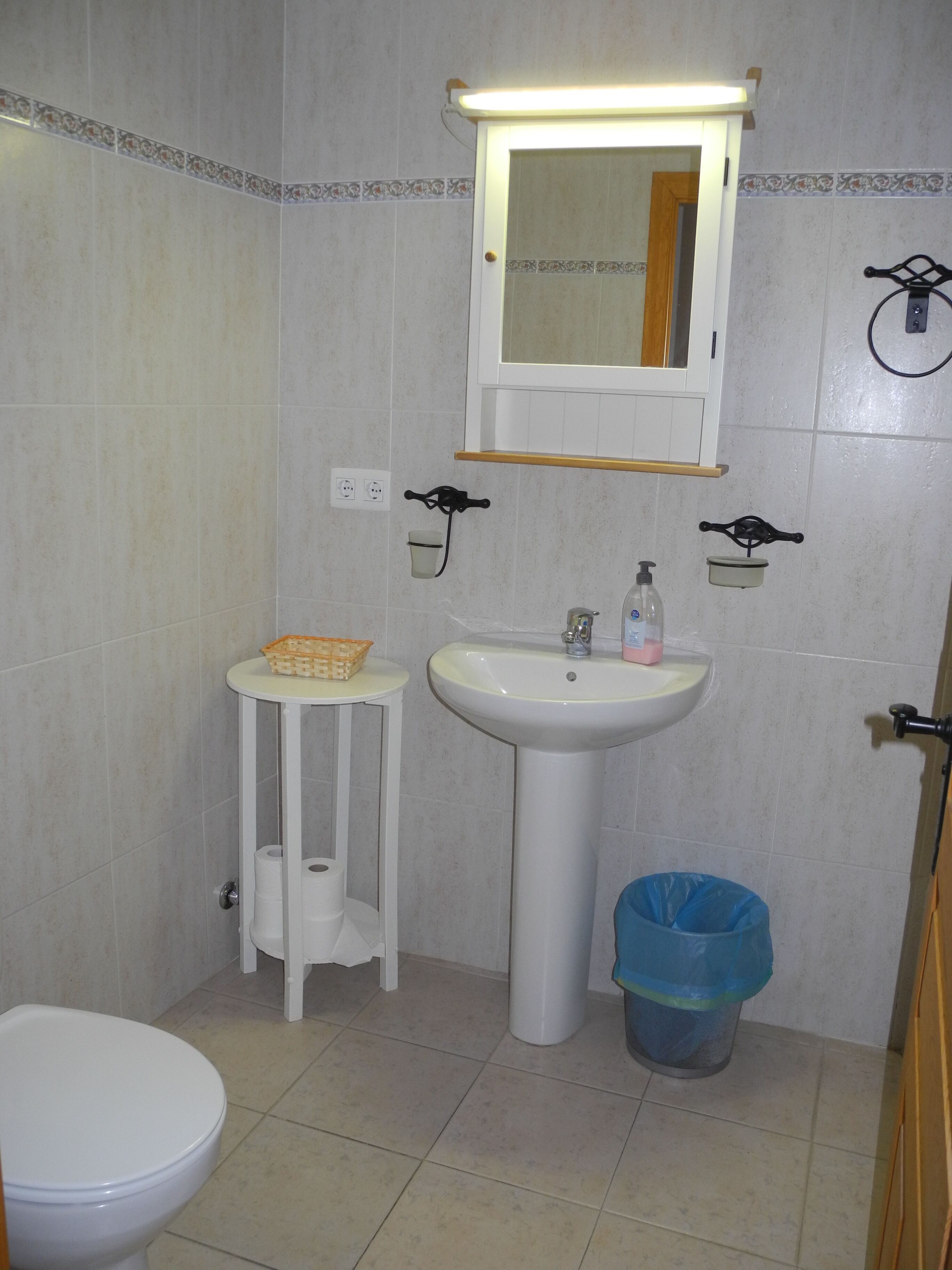 Un baño con inodoro, lavamanos, espejo y un cubo de basura.