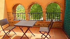 Terraza con mesa, dos sillas, baranda y tres ventanales arqueados con vistas a zonas verdes.